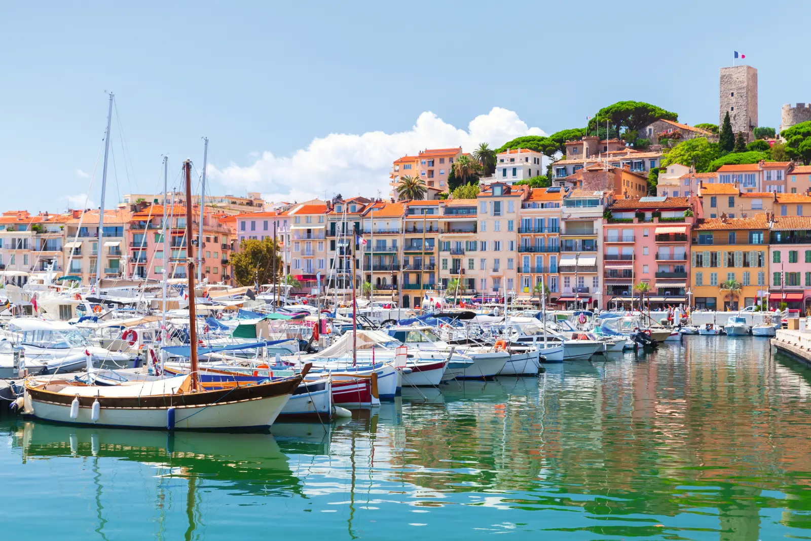 Barche nel porto davanti a edifici colorati su più piani e una vecchia torre su una collina.