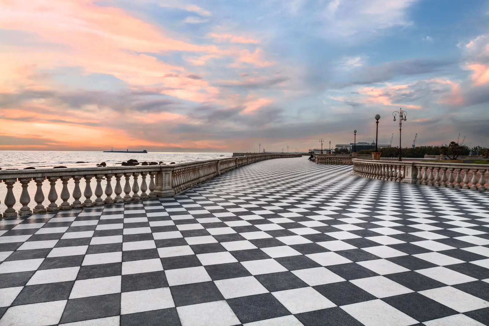 Promenade with a chequerboard-patterned floor at sunset by the sea in Livorno, Italy.