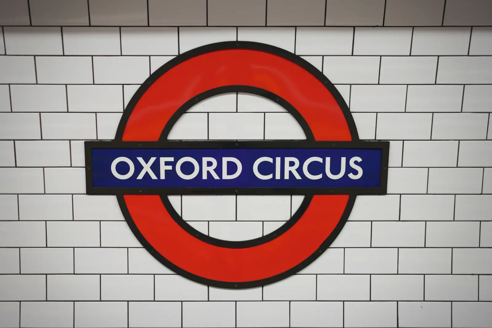Cartello rotondo della metropolitana di Oxford Circus davanti a una parete di piastrelle bianche.