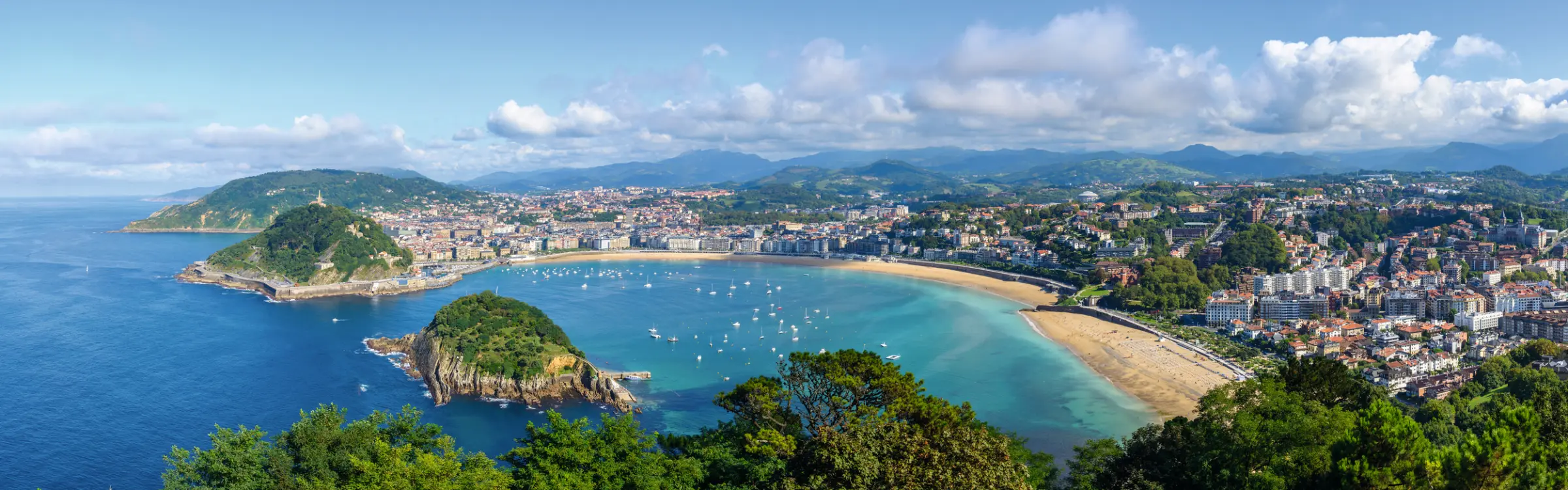 Panoramablick auf eine Küstenstadt mit Sandstrand und Hafen bei klarem Himmel.