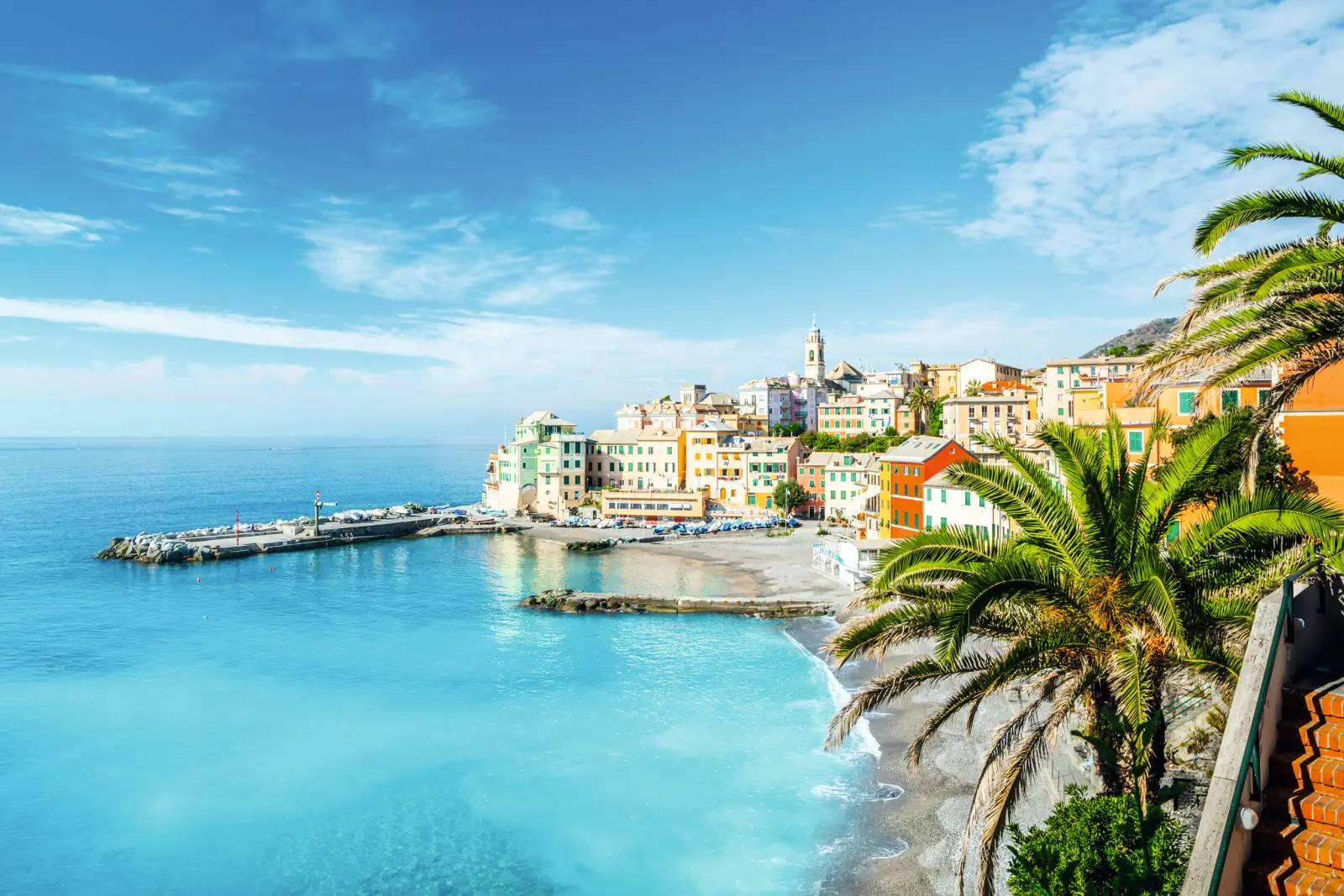 Costa con edifici colorati, palme e mare cristallino sotto un cielo azzurro.