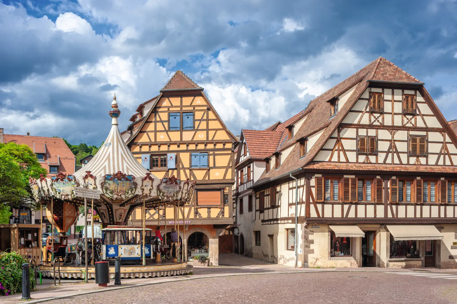 Maisons à colombages et manège sur une place sous un ciel nuageux.
