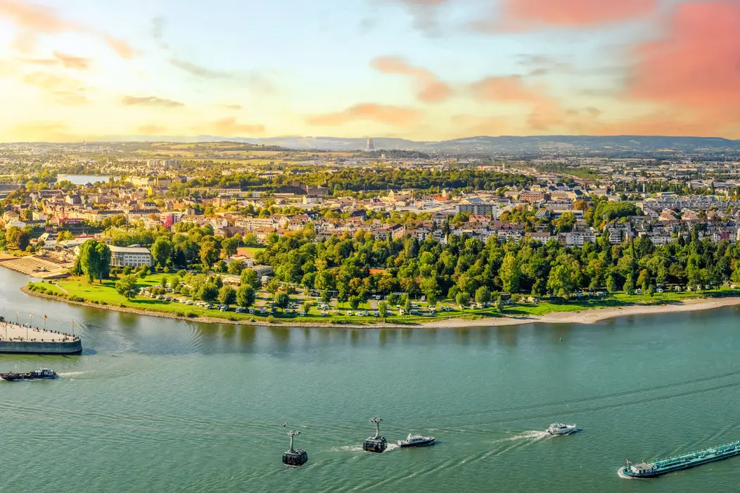 Vue panoramique d’un paysage fluvial au coucher du soleil, avec ville et bateaux.
