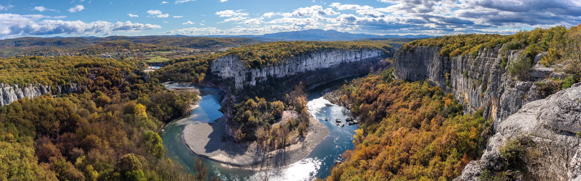 Rivière dans une gorge, entourée de collines boisées et de feuillage automnal.