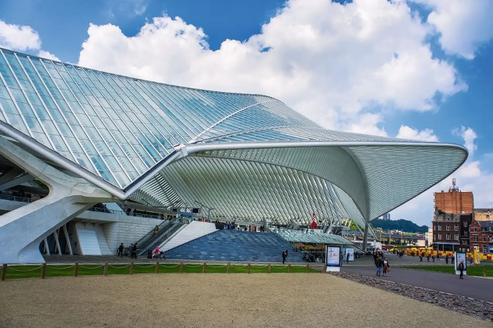 Stazione futuristica con facciata di vetro ondulata e nuvole nel cielo.