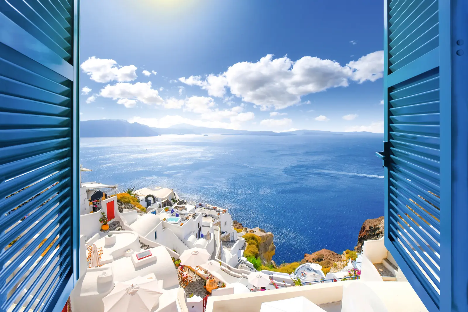 Blick aus einem Fenster auf Santorini mit weißem Dorf und blauem Meer.