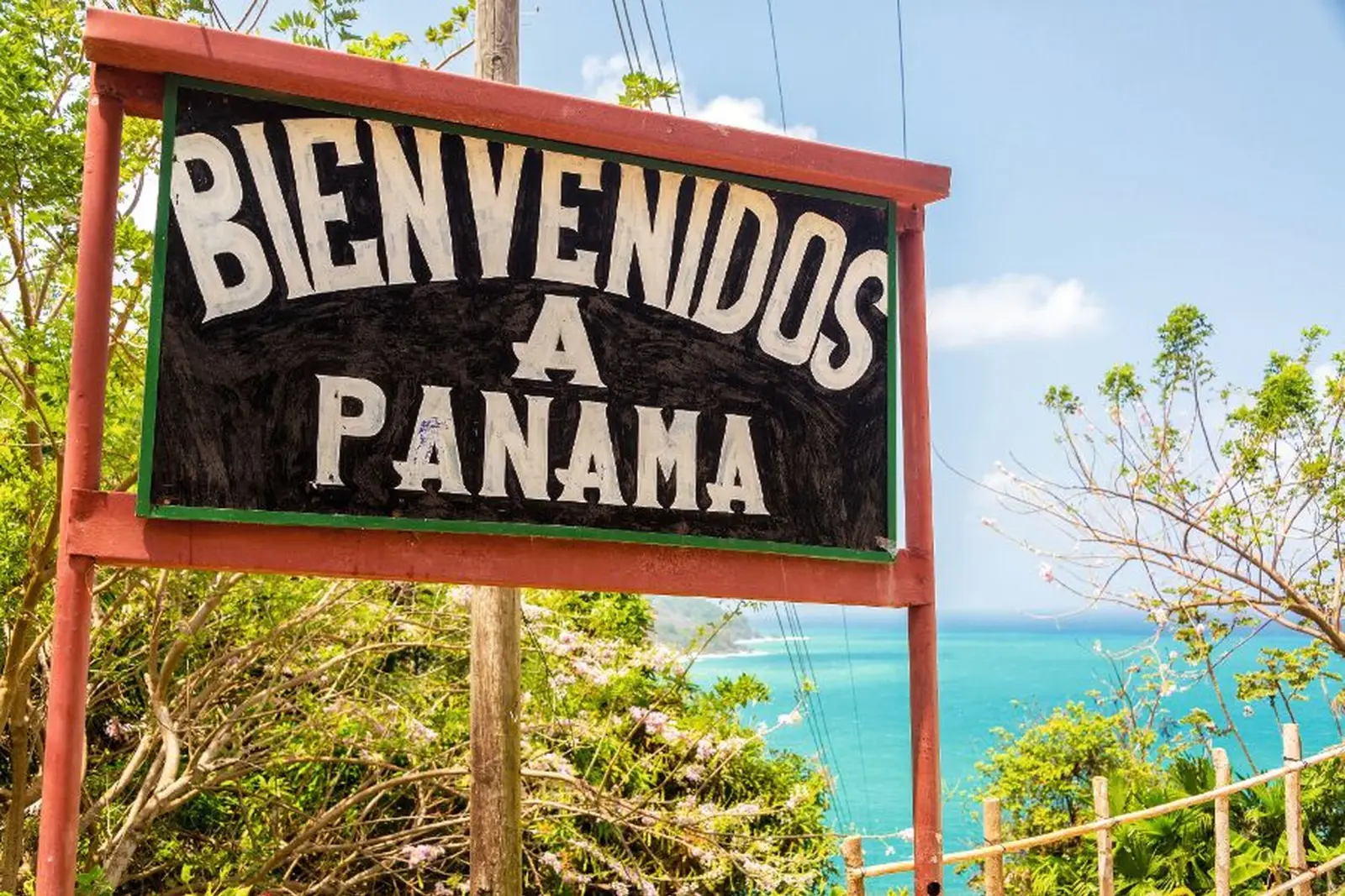 Panneau de bienvenue au Panama devant un paysage tropical et la mer.
