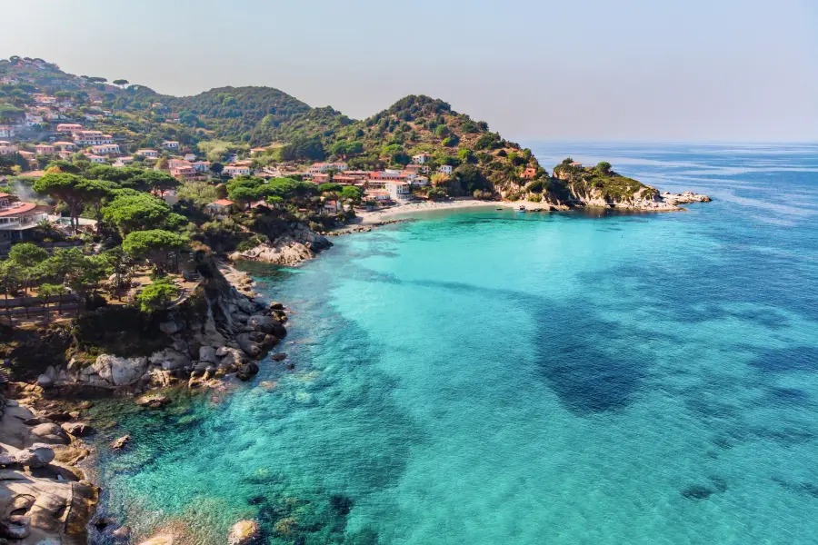 Küste mit blauem Meer und bewaldetem Hügel im Hintergrund.