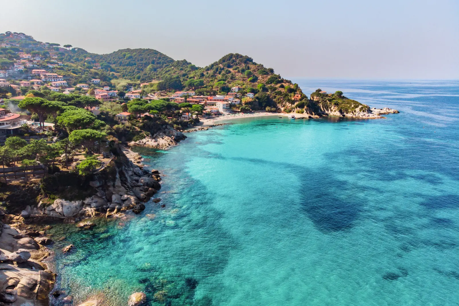 Costa con mare blu e colline boscose sullo sfondo.