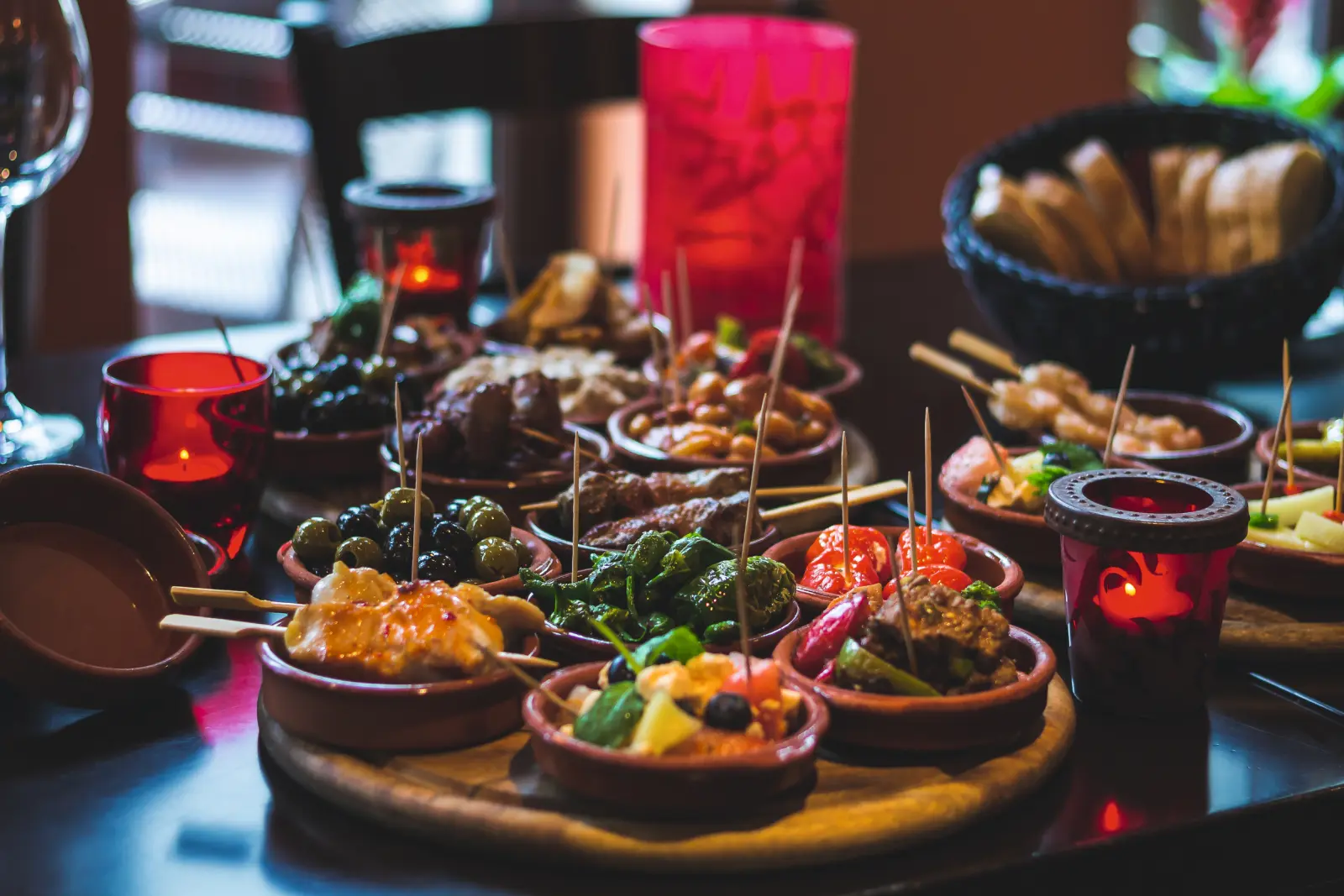 Verschiedene Tapas auf einem Tisch mit Kerzen und Brot im Hintergrund.