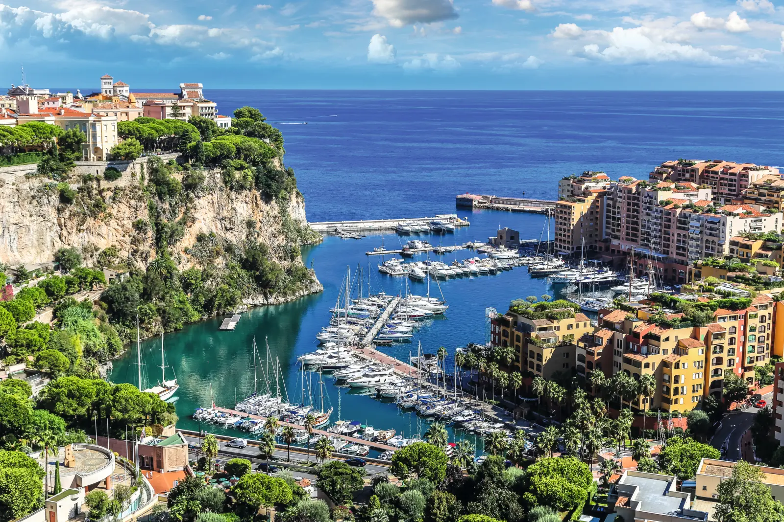 Harbour of Monaco with yachts and buildings in front of blue sea and sky.