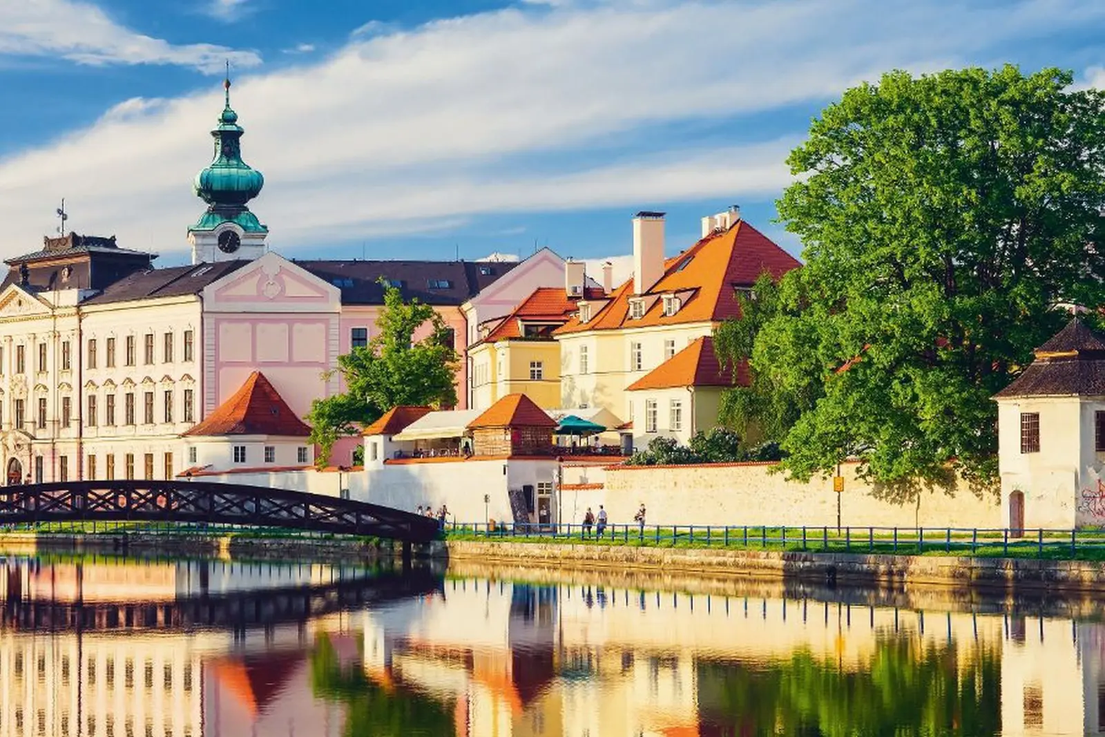 Colourful historic buildings with a tree and river in the foreground.
