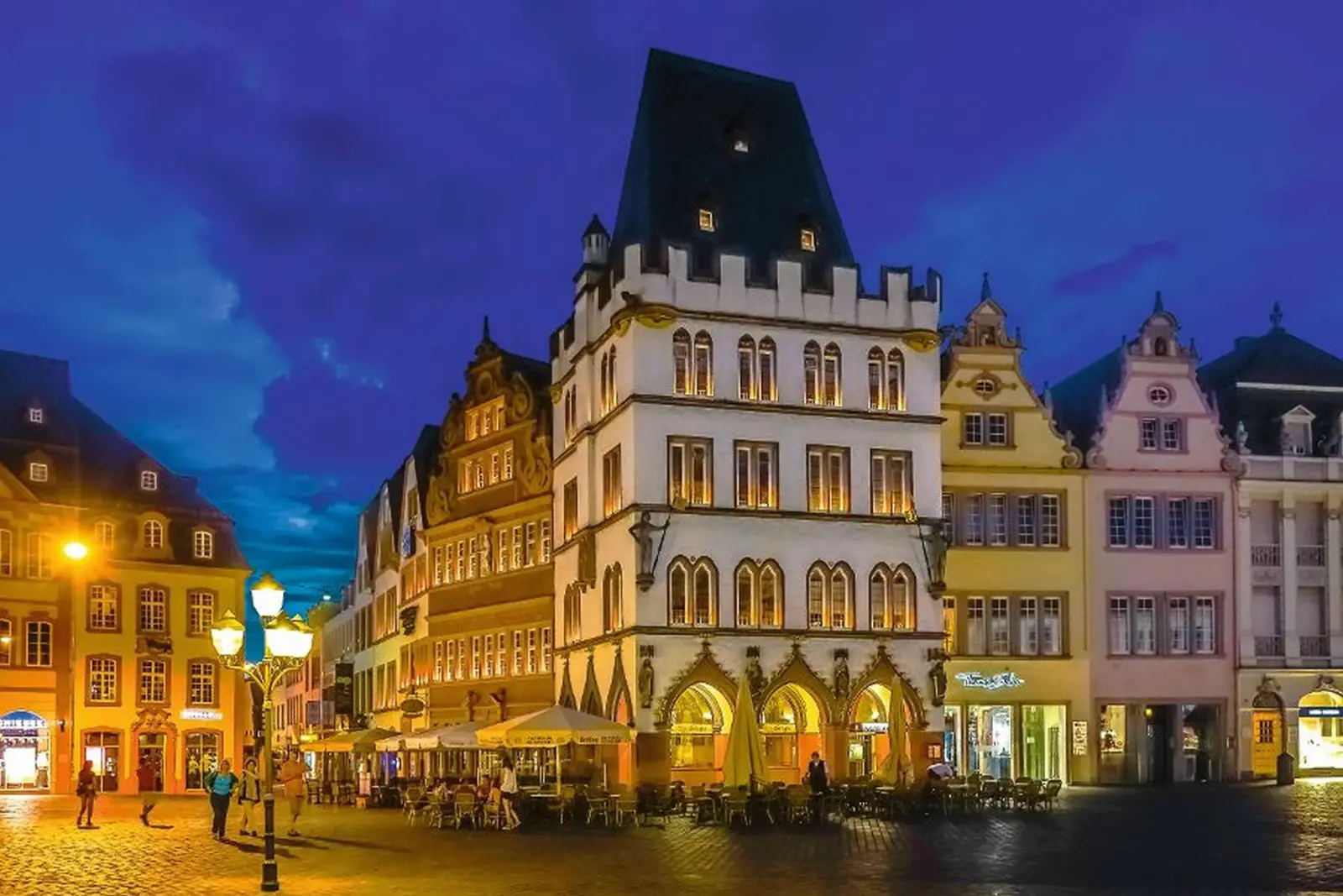 Historic building at night on a busy square with café guests.