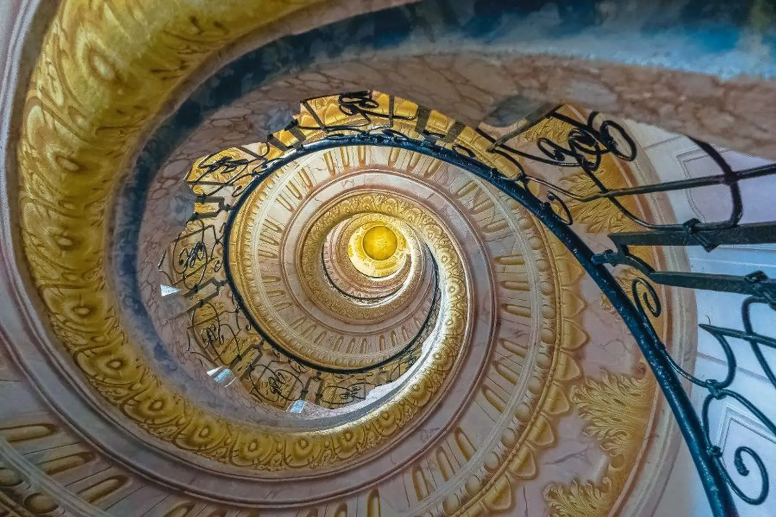 Looking up into an ornately decorated spiral staircase with wrought-iron banister.