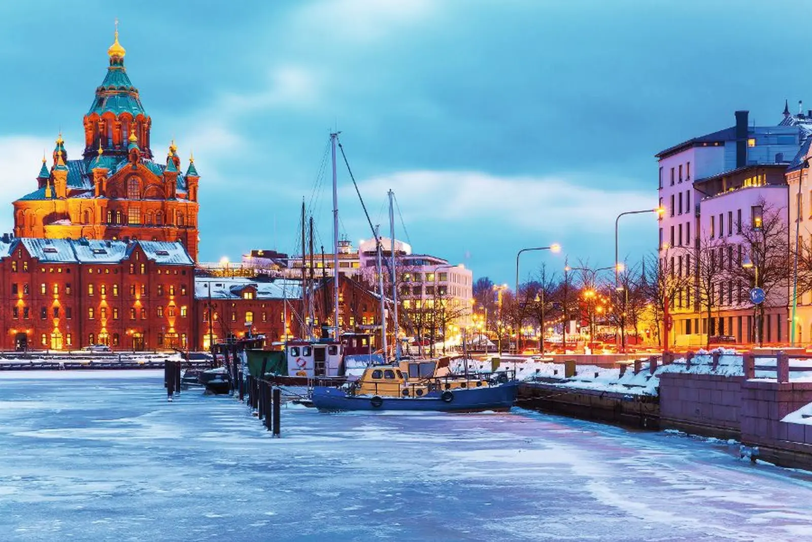 Snowy harbour with illuminated church and boats at dusk.