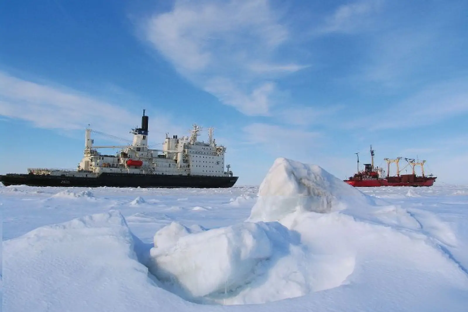 Two ships in an Arctic landscape, surrounded by ice and snow under a blue sky.
