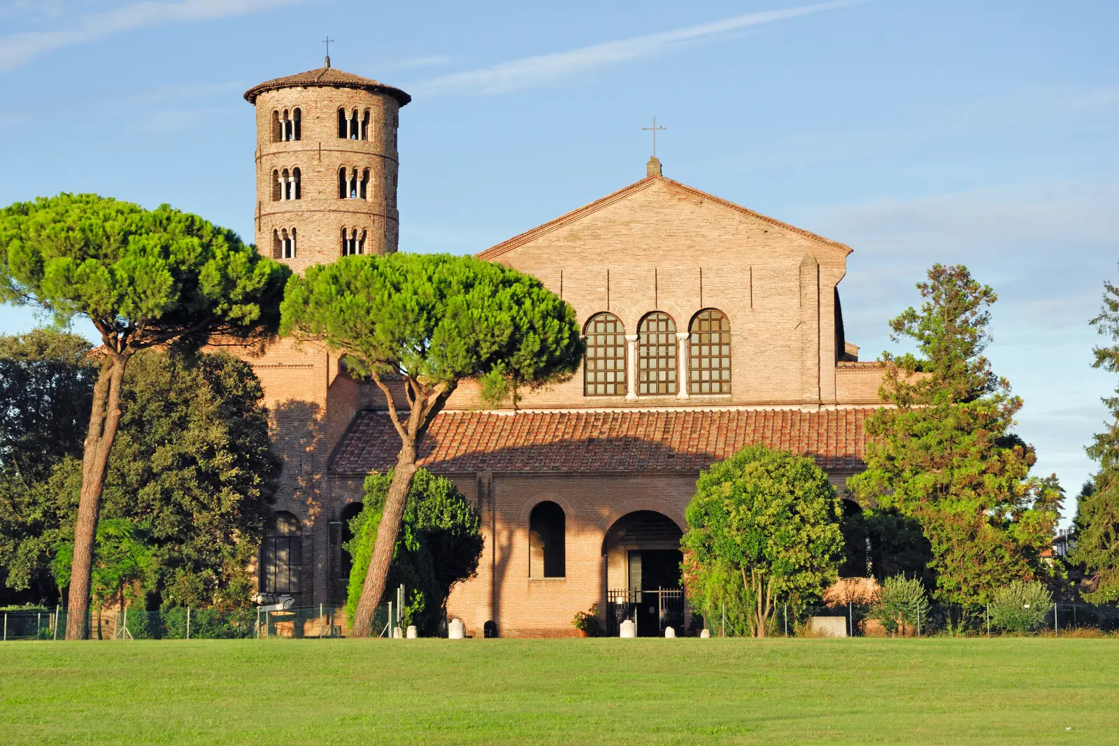 Chiesa con torre rotonda, circondata da alberi, sotto un cielo sereno.
