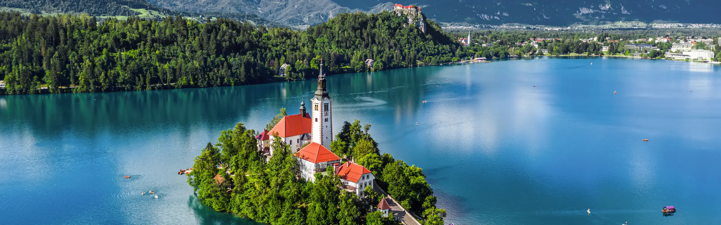 Insel mit Kirche im türkisblauen See, umgeben von Bergen und Wäldern.