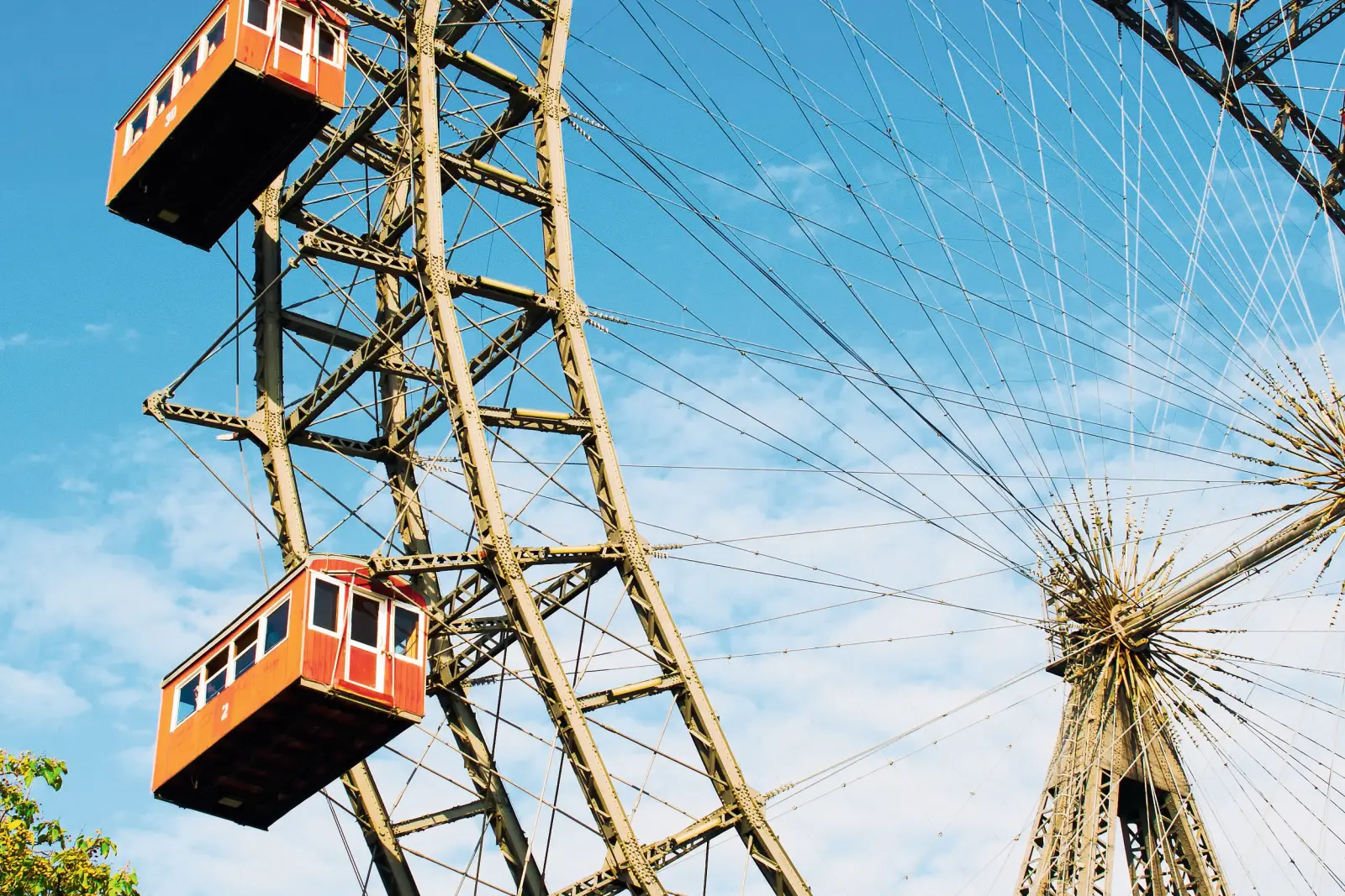 Historic Ferris wheel with red gondolas against a blue sky and green trees.