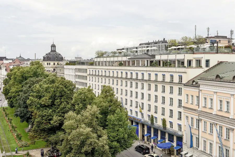 Facciata dell'hotel Bayerischer Hof a Monaco di Baviera con alberi e strada.