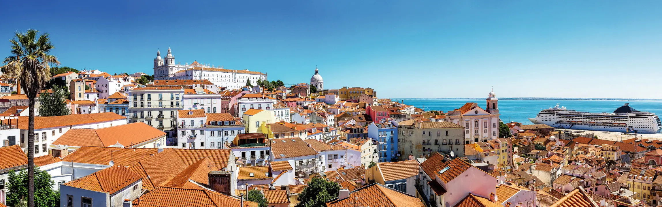 Vista panoramica su Lisbona con tetti rossi e nave da crociera sul mare.