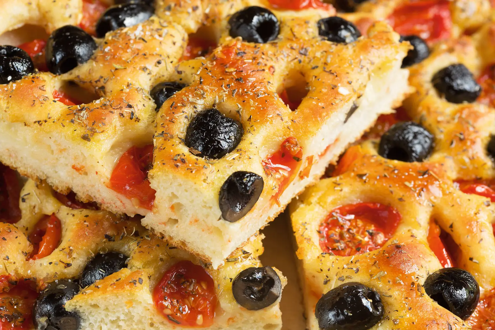 Focaccia con olive nere e pomodori secchi, cosparsa di erbe aromatiche.
