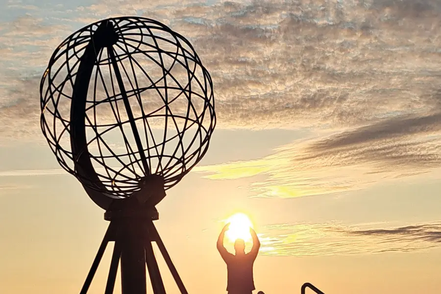 Persona presso il monumento del Globo a Capo Nord, che tiene il sole, al tramonto.
