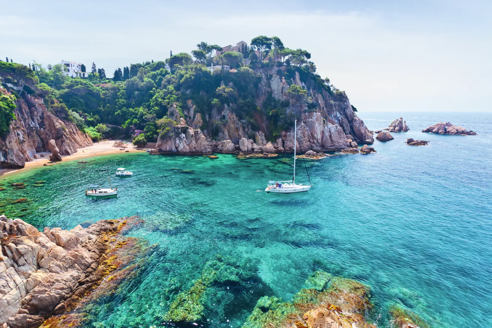 Barca a vela davanti a una costa rocciosa con acqua blu cristallina e piccole baie