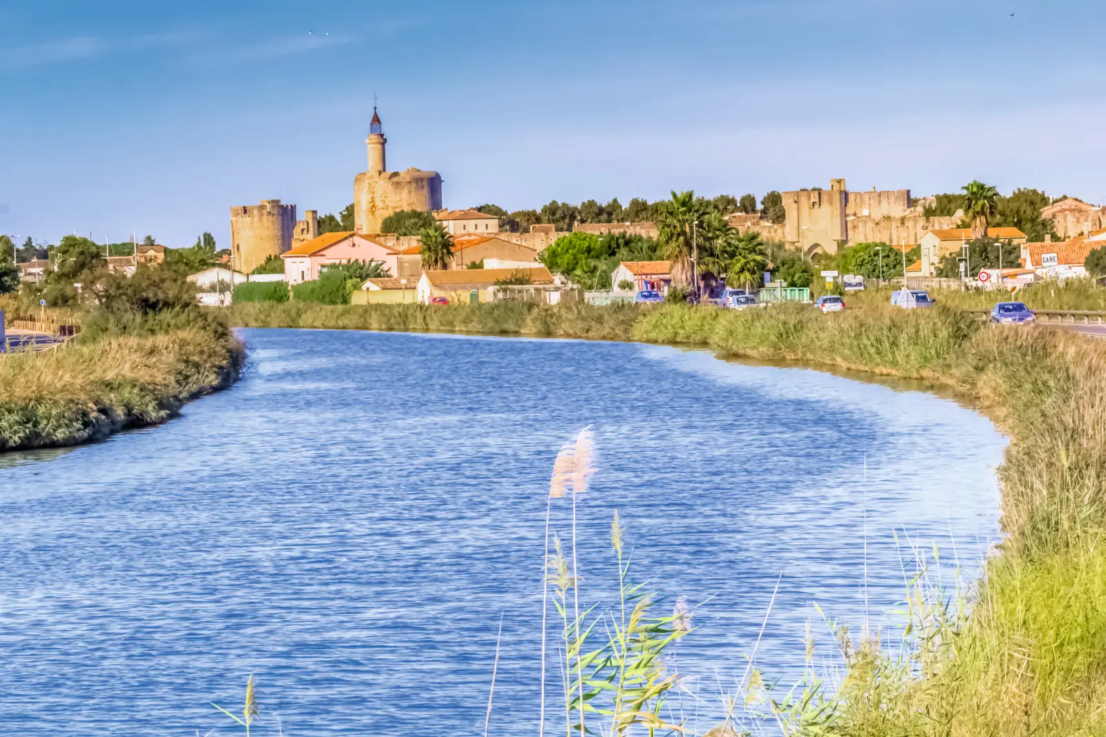 Veduta della città con torri del castello e fiume in primo piano sotto il sole.