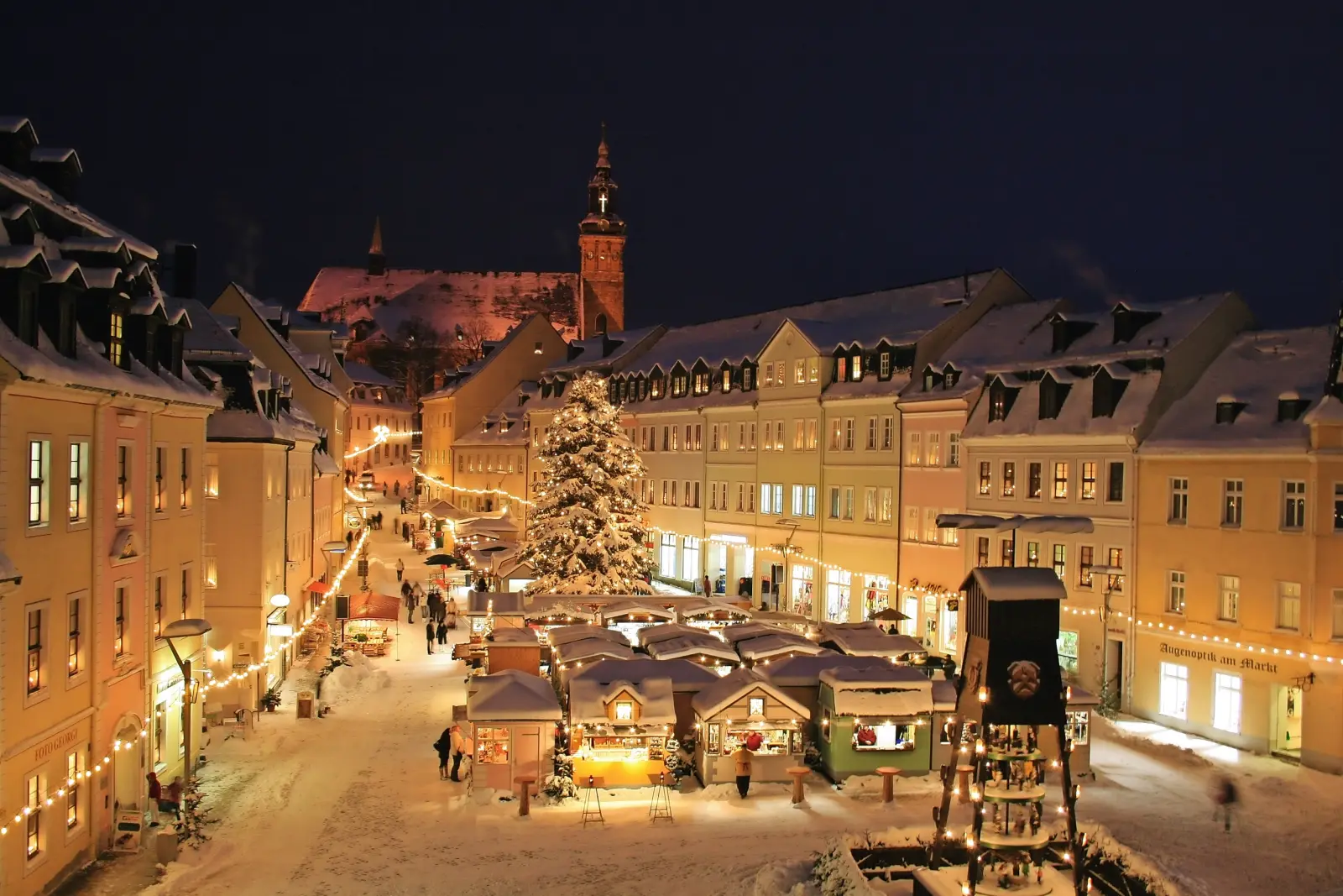 Snowy Christmas market in an illuminated old town at night.