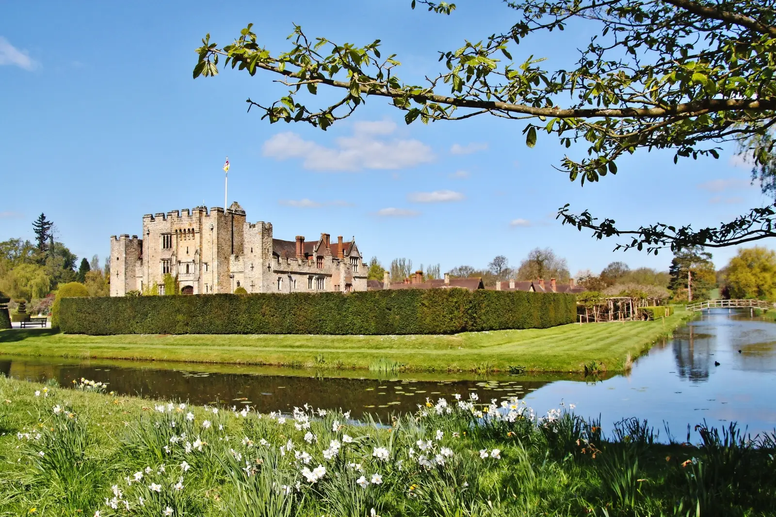 Historic castle with moat and gardens in sunny weather.