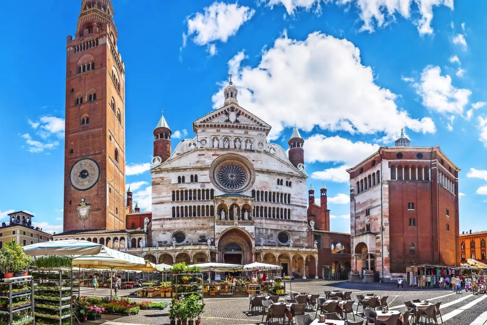Storica piazza del Duomo con cattedrale e campanile sotto un cielo azzurro e bancarelle del mercato.