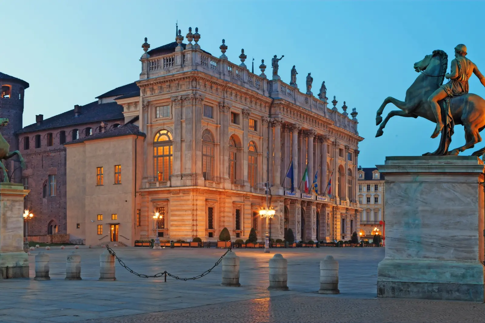Edificio storico con decorazioni, fiancheggiato da statue equestri in una scena serale.