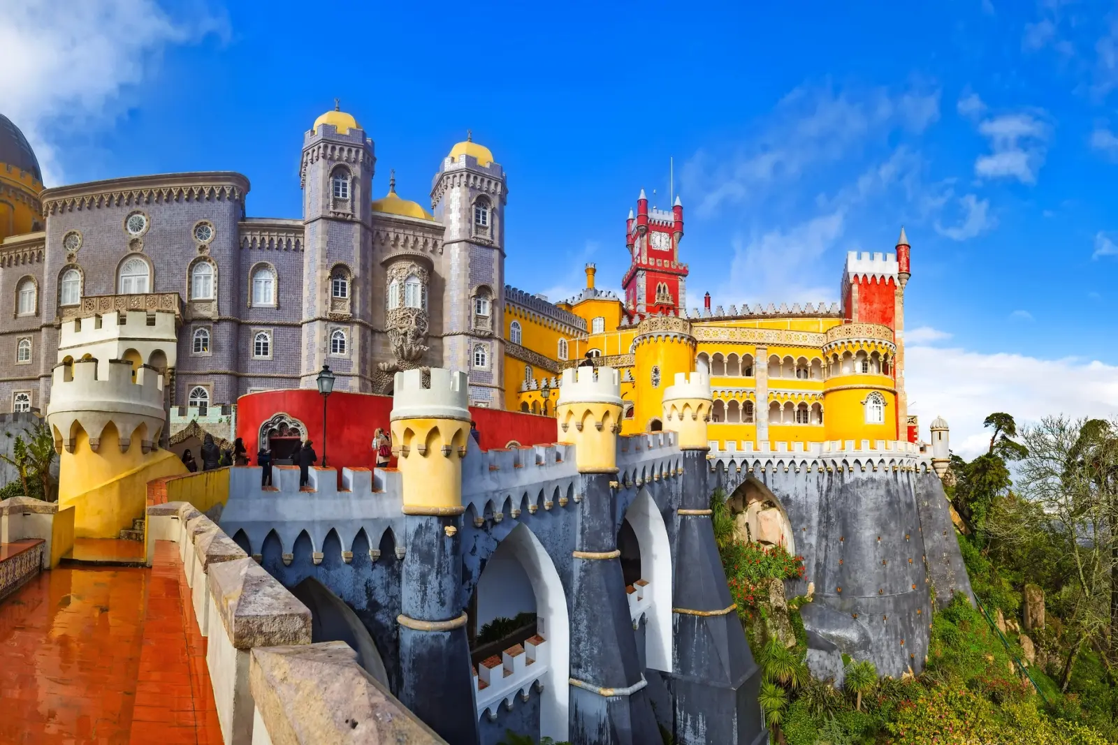 Buntes Schloss auf Hügel mit blauen Himmel und grüner Landschaft.