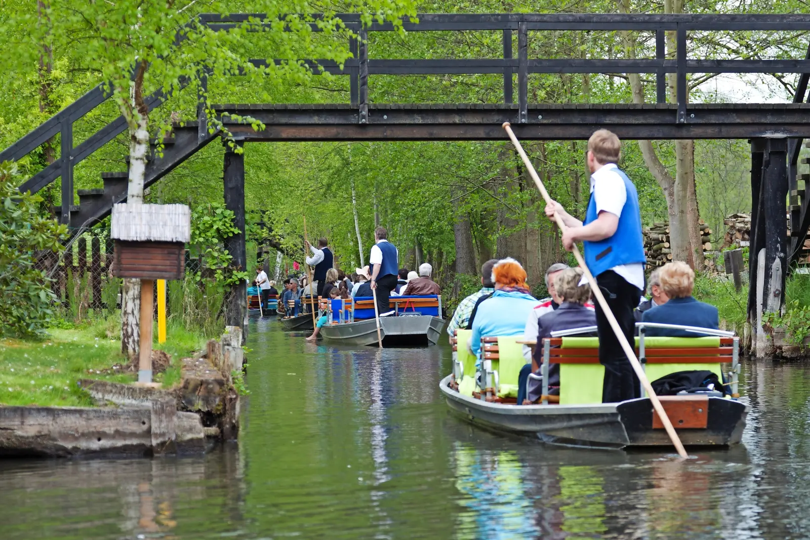 Des personnes en barque traversent un canal vert bordé d'arbres.
