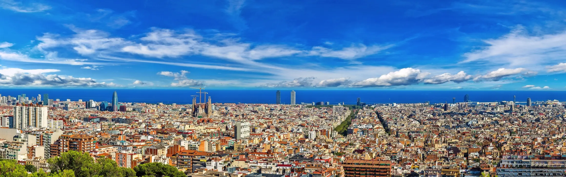 Panorama d’une ville sous un ciel bleu, avec des nuages à l’arrière-plan.