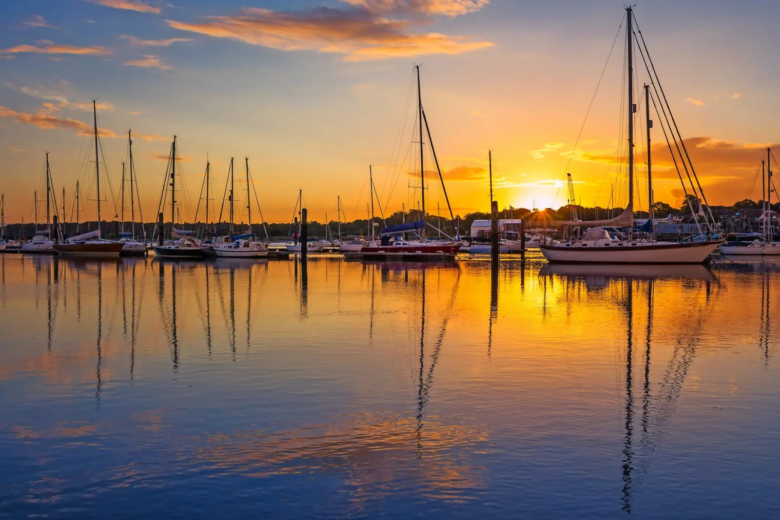 Barche a vela nel porto al tramonto con riflesso sull'acqua