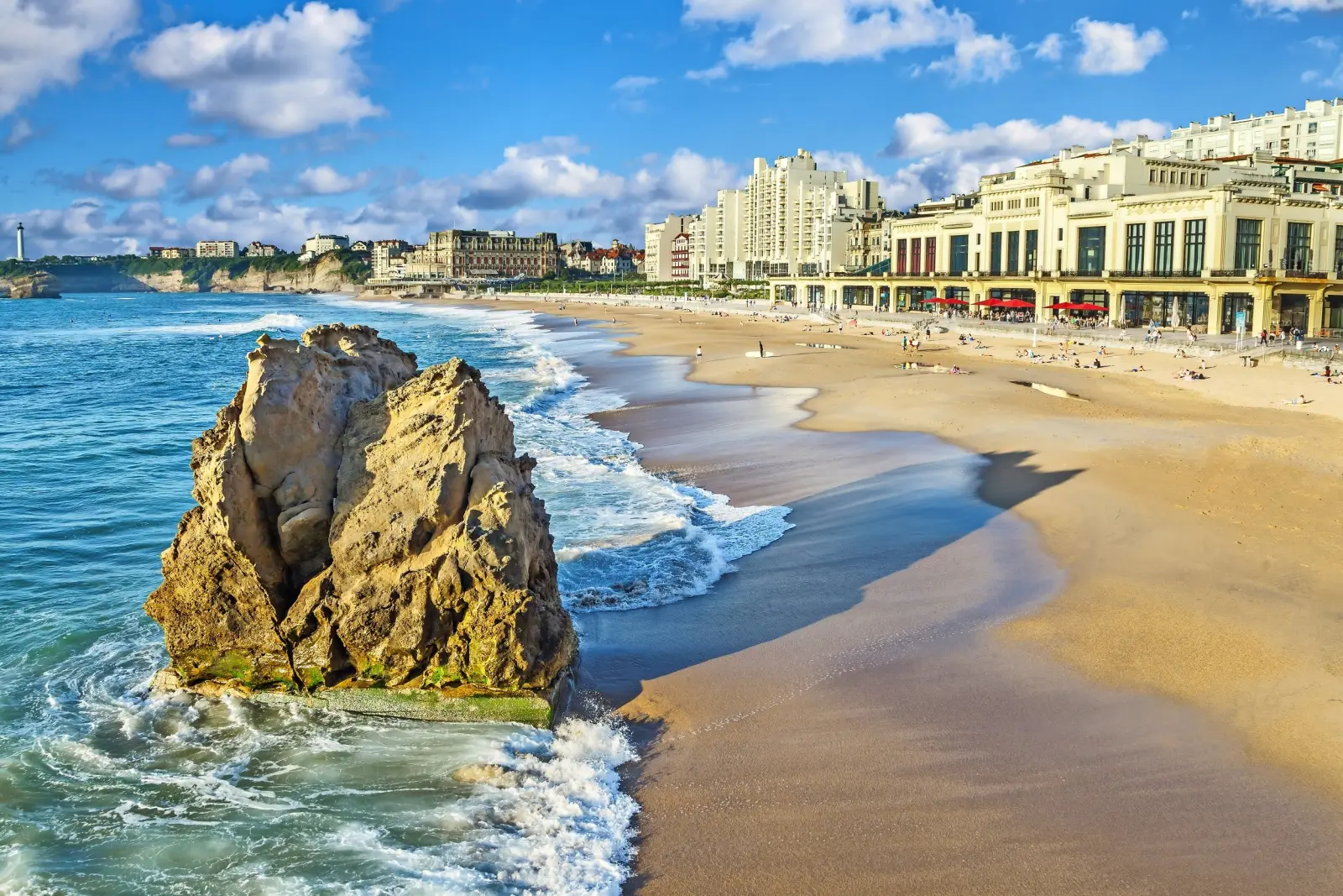 Spiaggia con scogliere, edifici cittadini e cielo azzurro sullo sfondo.