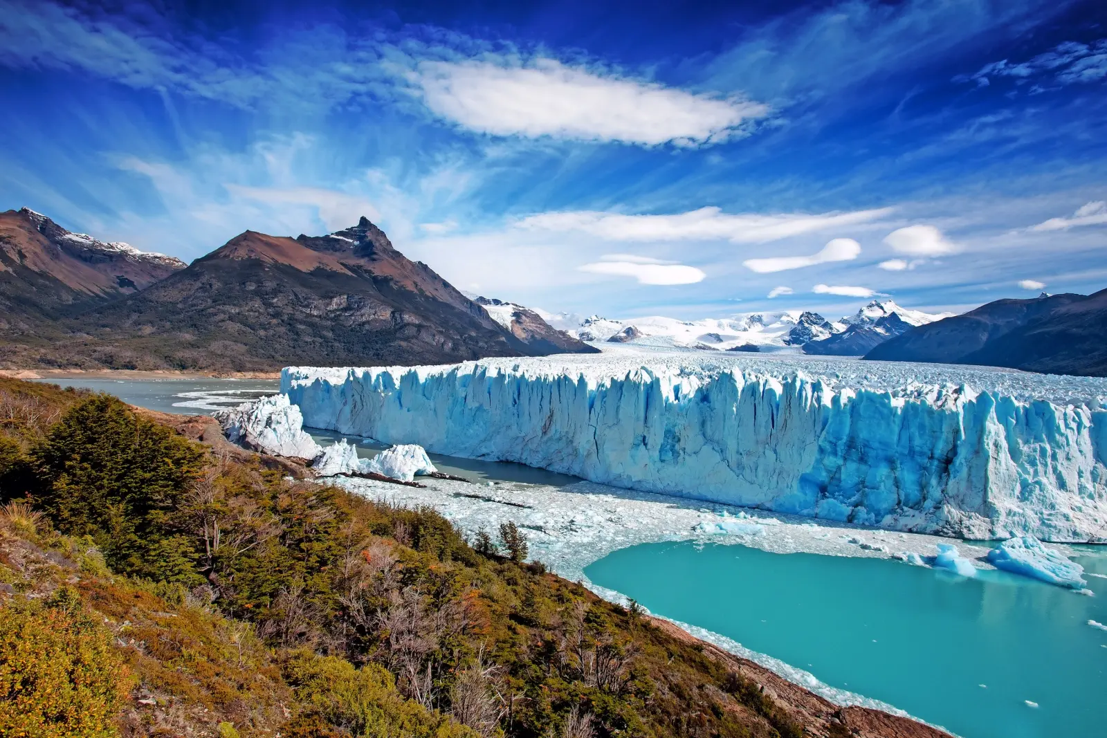 Ghiacciaio in un paesaggio montano accanto a un lago turchese, con cielo azzurro.