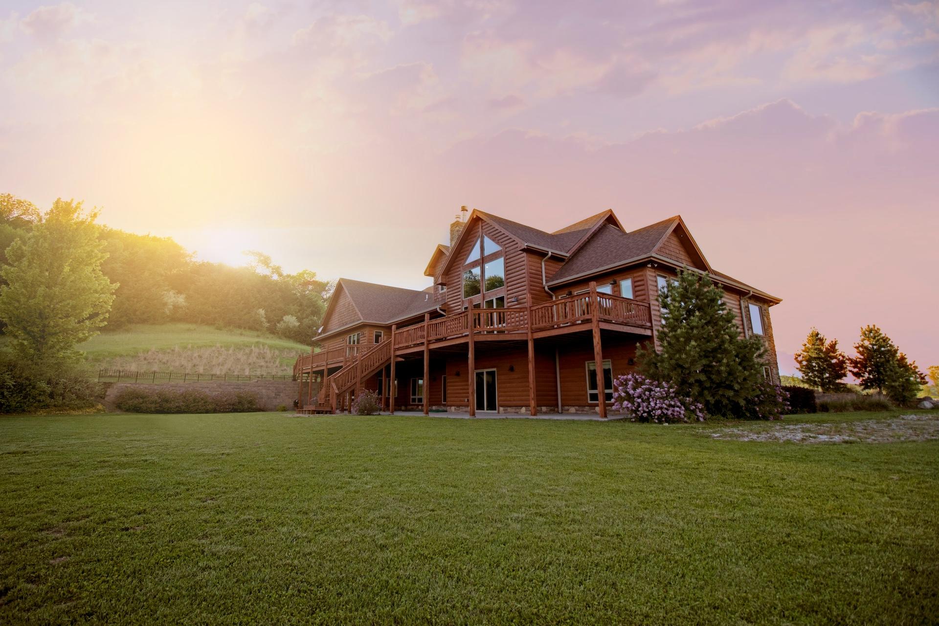 A two-story wooden house with multiple balconies and a spacious lawn, set against a sunset sky.