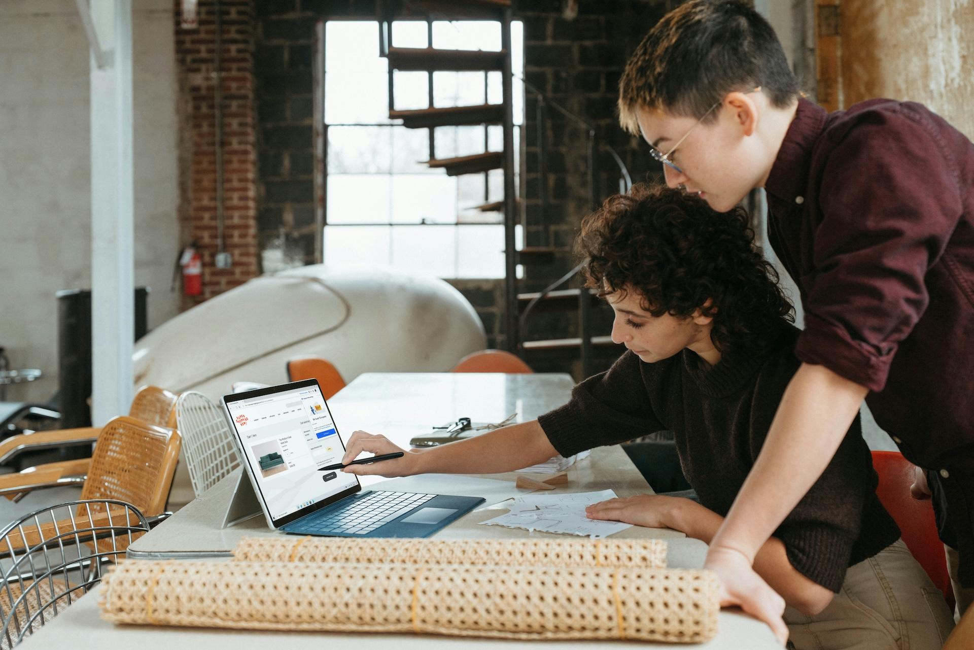 Two individuals working collaboratively on a laptop in a modern workspace.