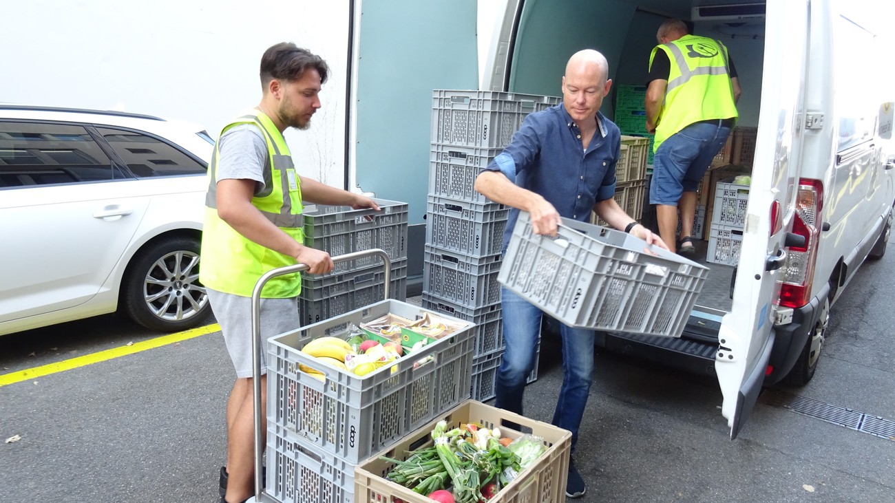 Des hommes déchargent une voiture de la Banque alimentaire suisse. Des caisses de denrées alimentaires sont empilées.
