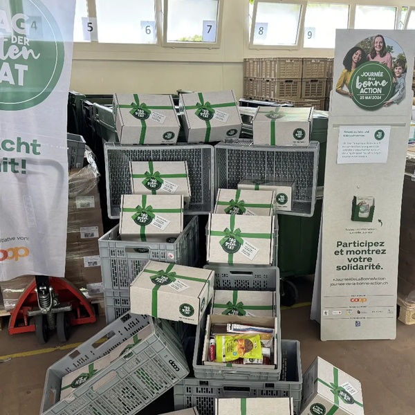Ausstellung von Spendenboxen in einem Regionallager Schweizer Tafel, mit Informationsbannern und Paletten mit Waren im Hintergrund.