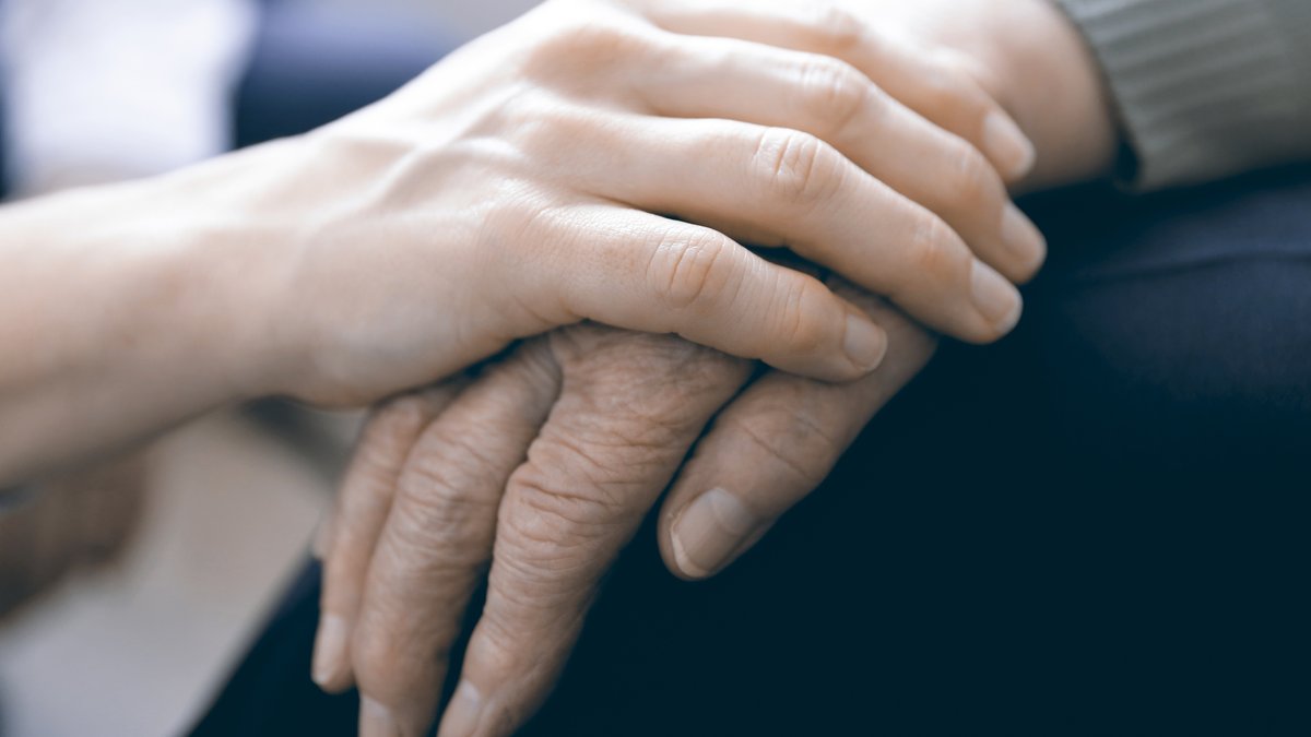 Pflegende Hand tröstend auf Hand von älterer Person