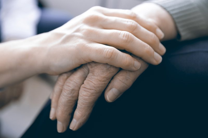 Pflegende Hand tröstend auf Hand von älterer Person