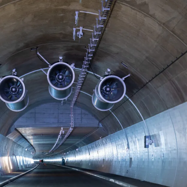 Drei grosse Lüftungsventilatoren an der Decke eines modernen Strassentunnels mit Betonwänden und Beleuchtung.