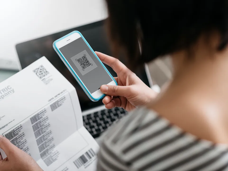 Frau, welche mit Ihrem Mobiltelefon einen QR-Zahlschein scannt