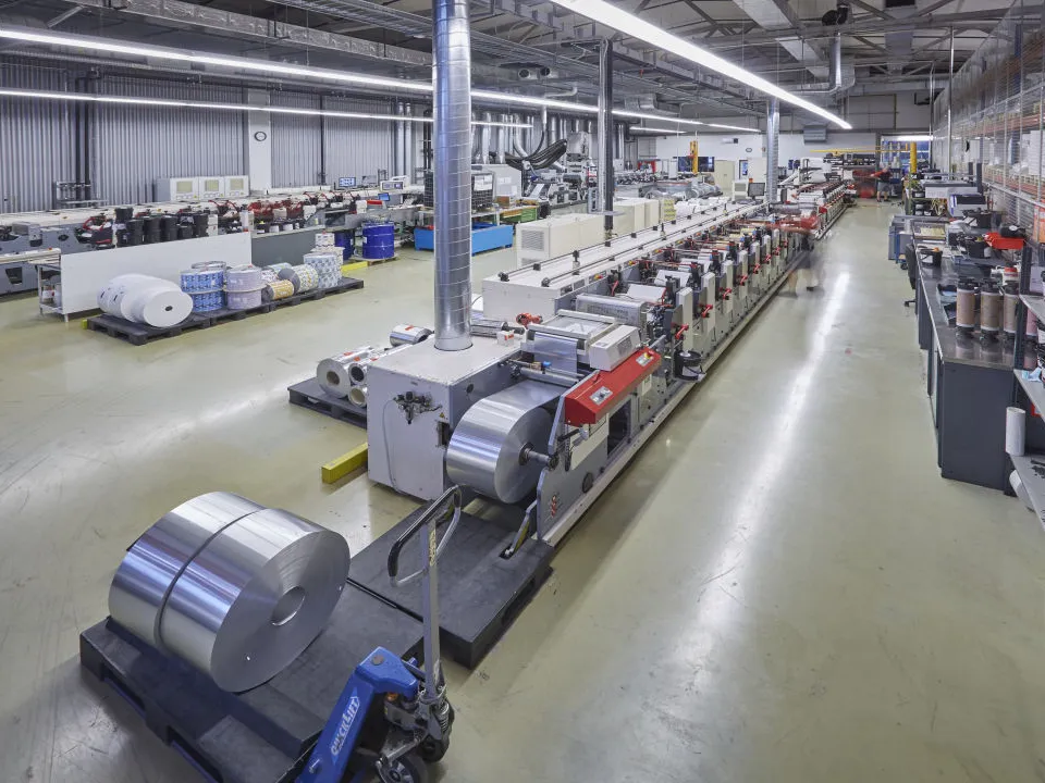 Eine industrielle Produktionshalle mit Maschinen und Etikettenrollen, die sich über den Raum erstrecken.
